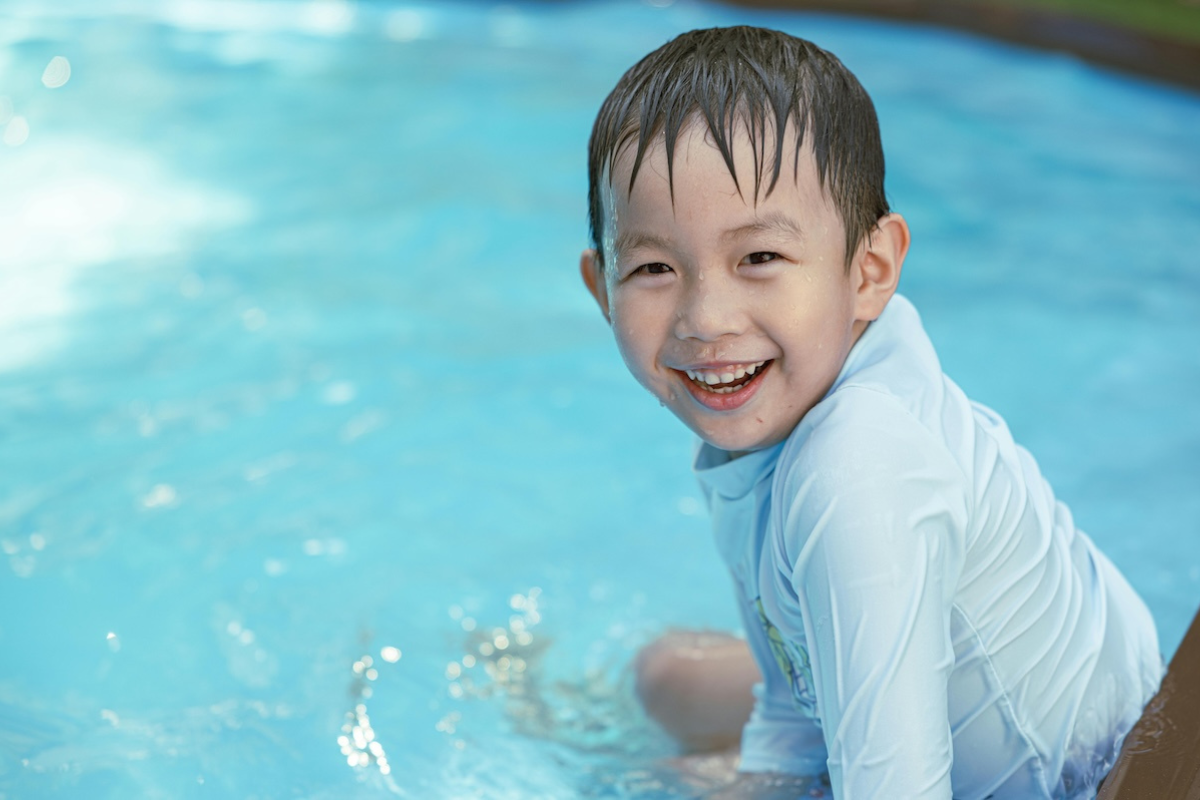 A kid sitting in a pool and smiling.