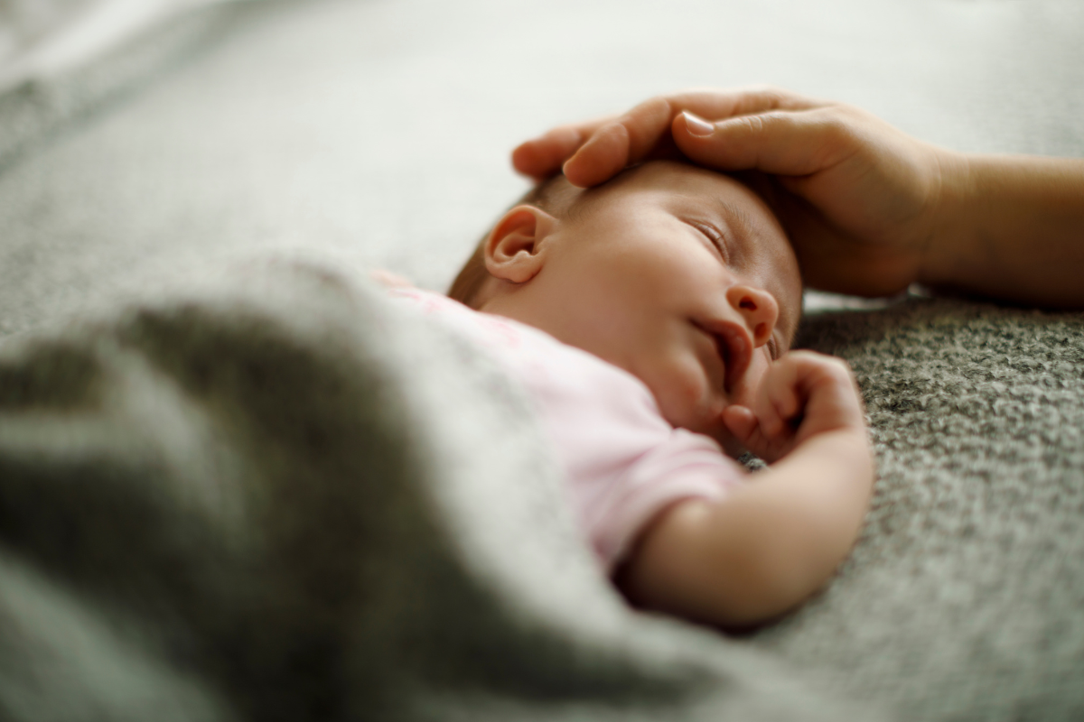 A baby sleeping while a hand is touching the baby's head.