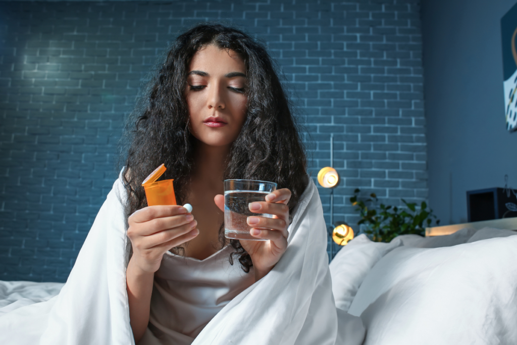 An unhappy-looking person sitting on bed and looking at pills.