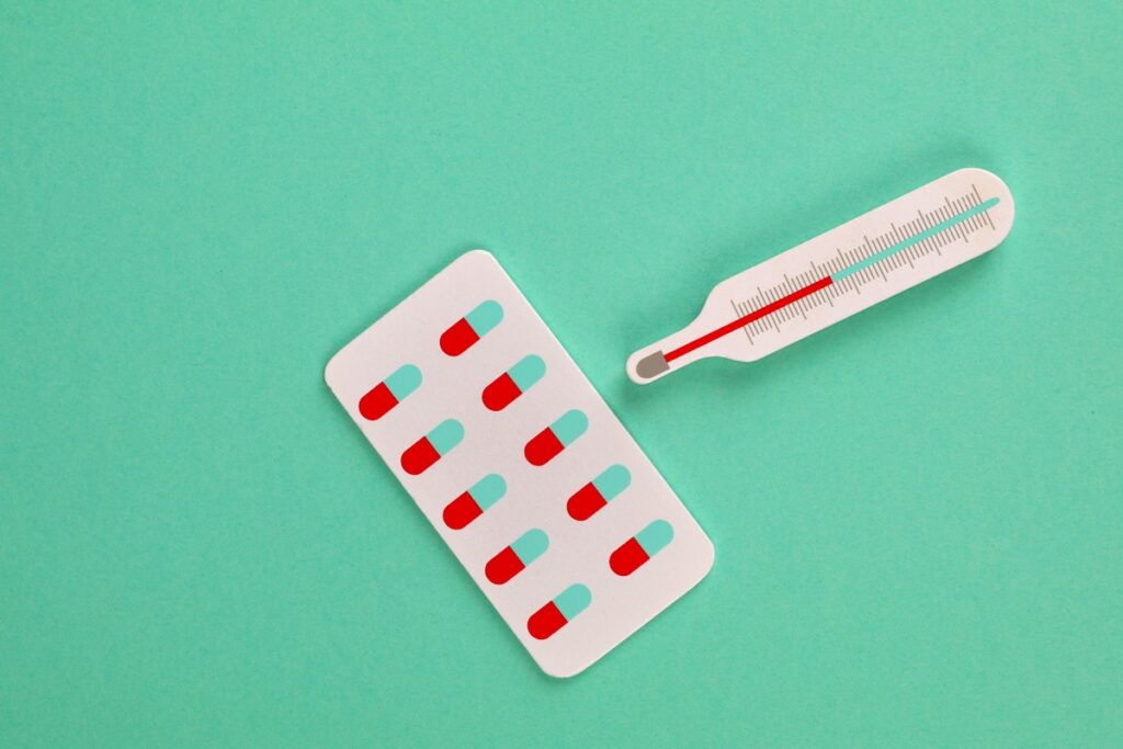 Medication Pills and Thermometer on Green Background