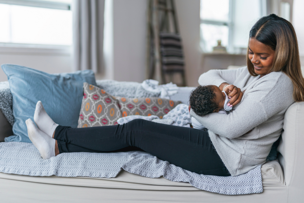 Mother holding her newborn, while cleaning their face and lounging on the couch.