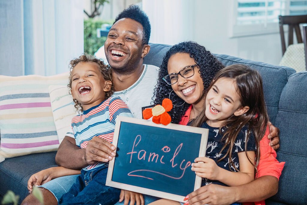 Happy, smiling family on a couch, daughter is holding a sign that reads "family."