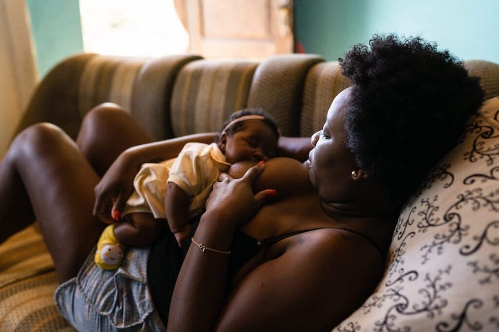 A mother reclines on a couch, snuggling her infant while her baby breastfeeds and dozes.