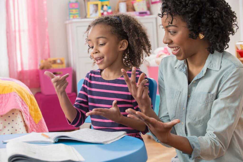 A parent and child smile and laugh as they count on their fingers in front of school notebooks.