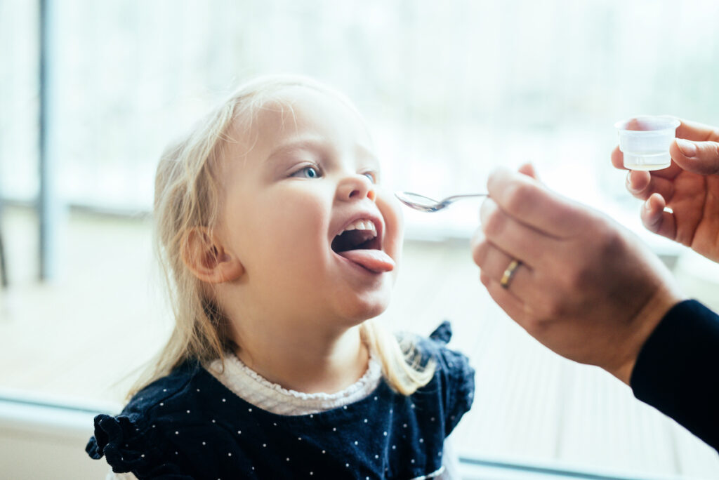 A mother gives a spoonful of medicine to her small child.