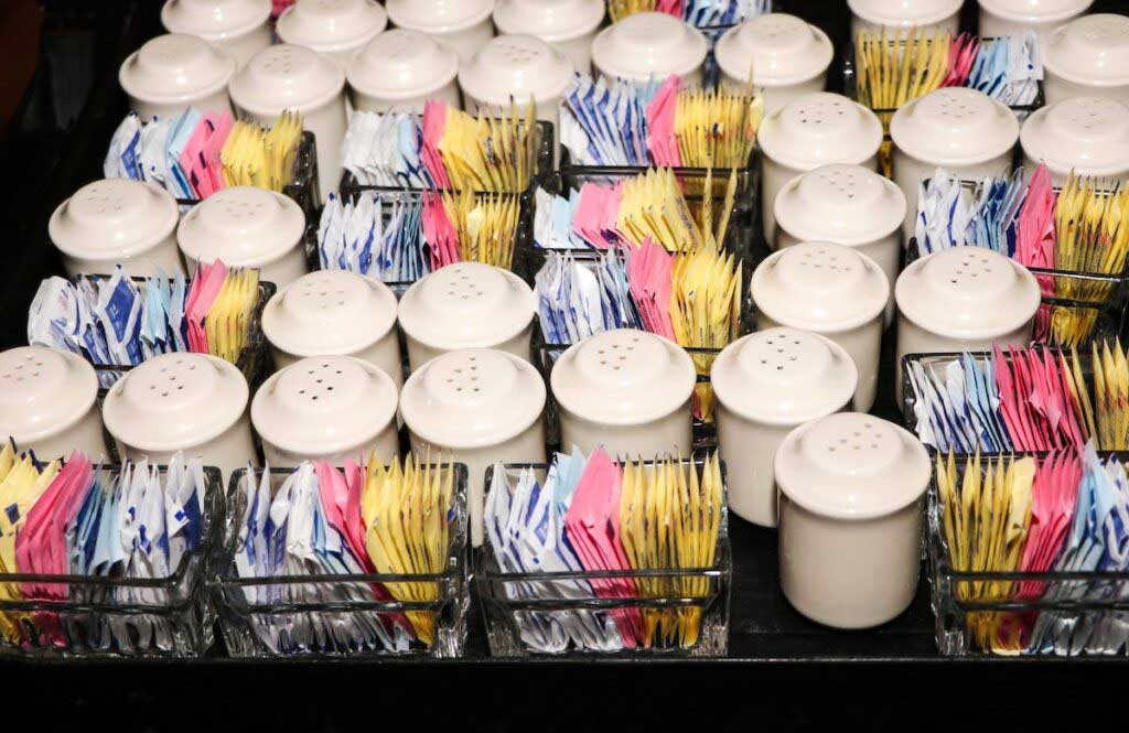 A photo of sugar containers and various sweeteners at a restaurant.