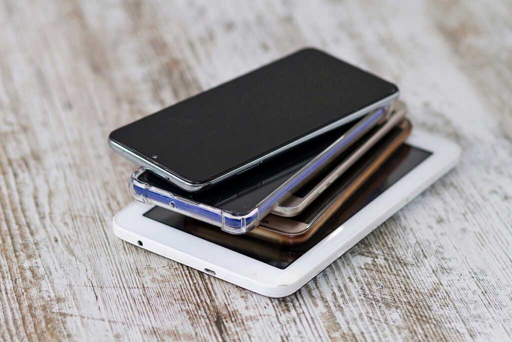 A stack of smarphones on a wood table.