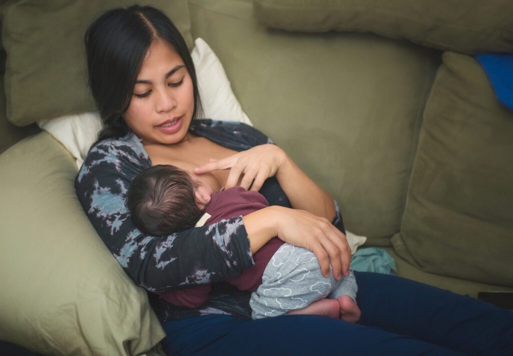 Woman nurses her baby while seated on a couch.