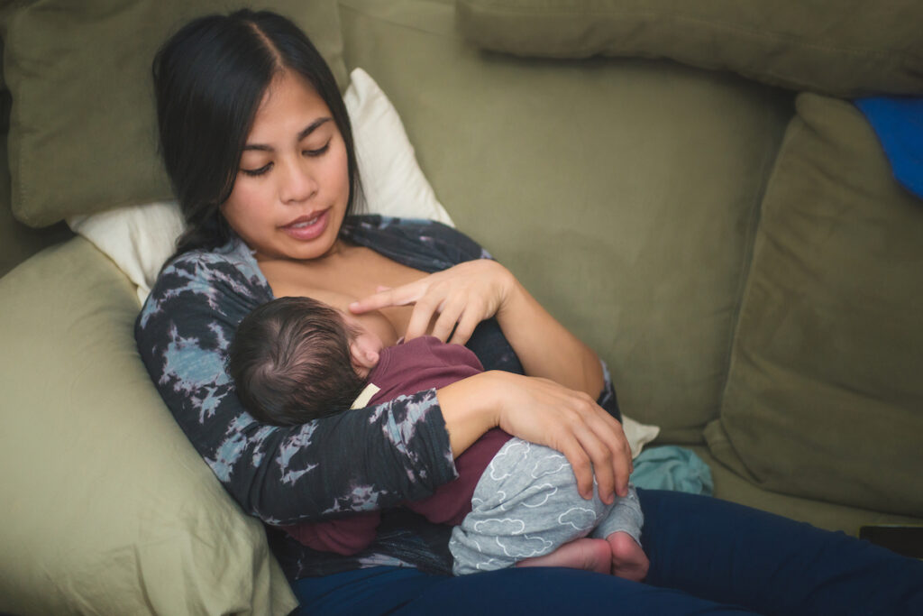 Woman nurses her baby while seated on a couch.