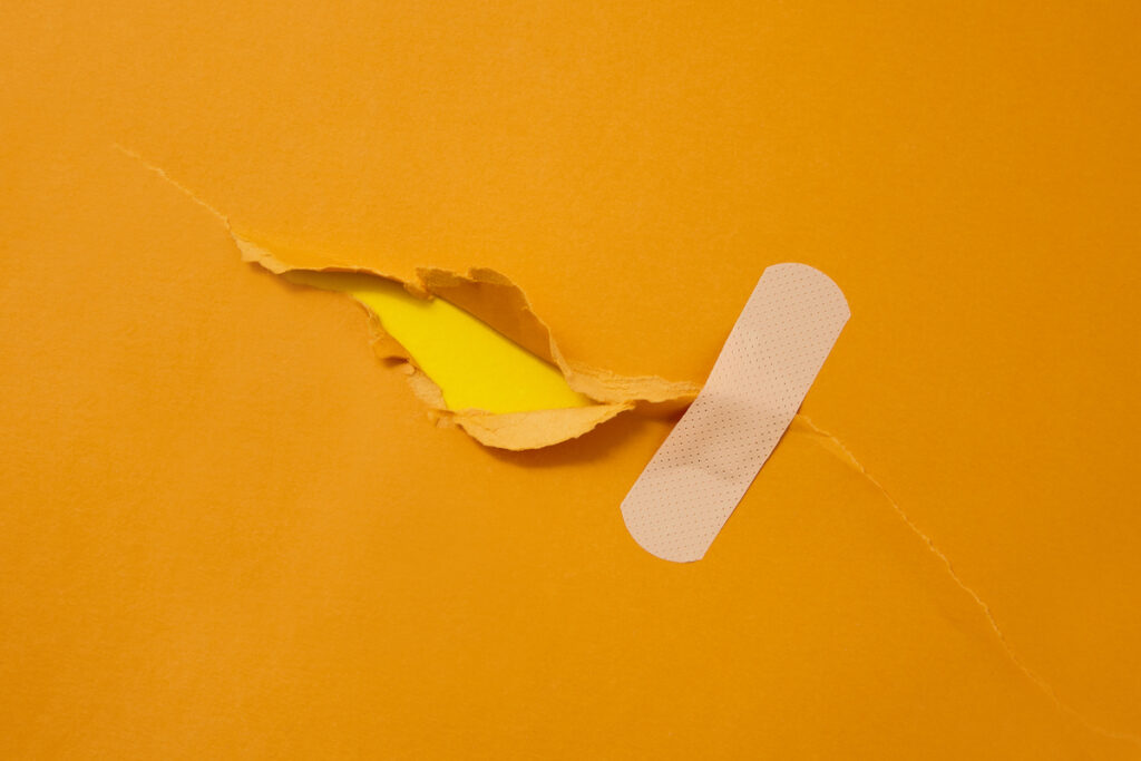 A bandaid is applied over a tear in a piece of orange paper.