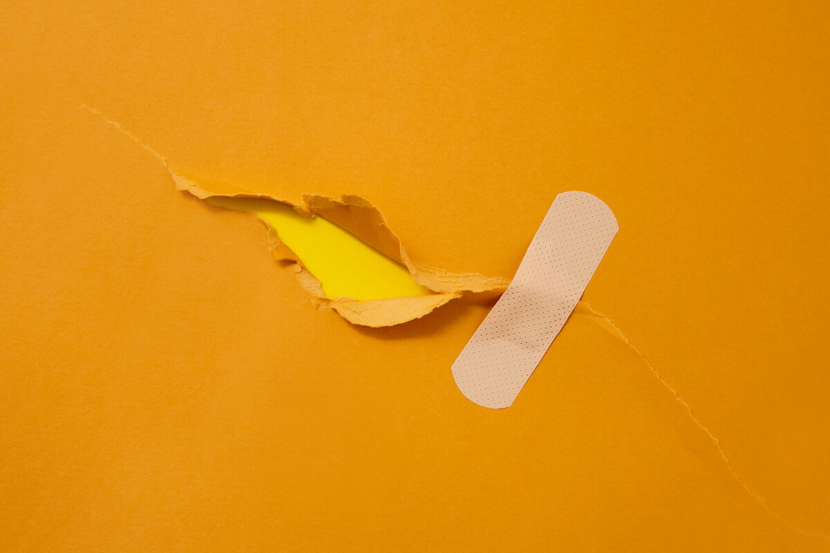 A bandaid is applied over a tear in a piece of orange paper.