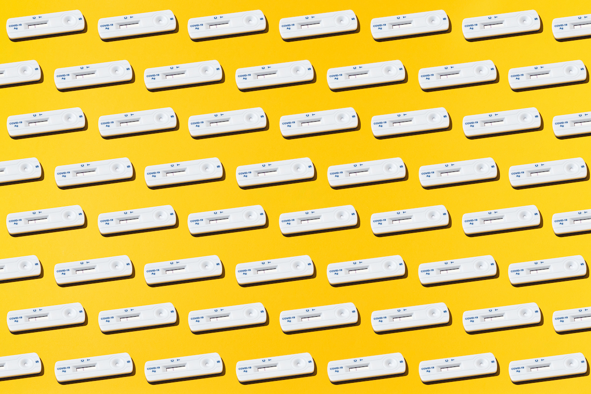 Covid-19 rapid antigen tests arranged in a pattern on a yellow background.