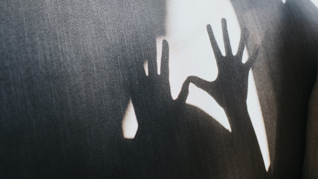 The shadow of two hands with fingers stretched out is projected on a wall.