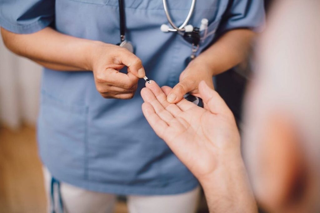 A nurse pricks the finger of an outstretched hand for a diabetes test.