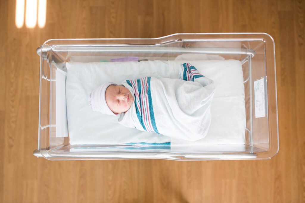 A one-day-old newborn infant sleeps in its crib in the hospital.