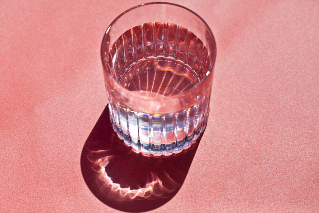 Close-up of a cut crystal glass of water reflecting on a pink background.