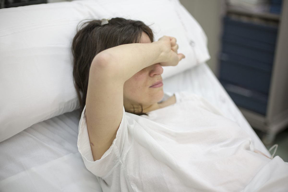 A pregnant person reclines on a hospital bed during labor with an arm slug over their head.