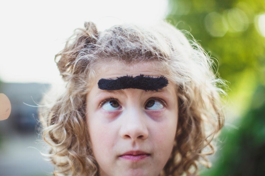 Close of a child crossing their eyes and wearing a funny unibrow sticker.