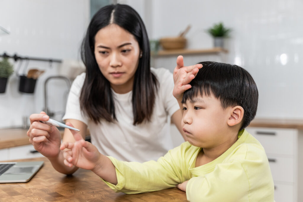 A mother takes her sick child's temperature at the kitchen table.