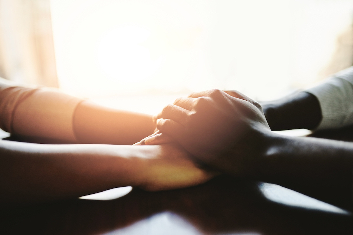 A close up of a couple holding hands at a table. The hands are in shadow, backlit by a window.