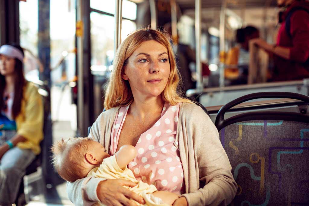 Mother breastfeeds on a city bus while looking out the window.