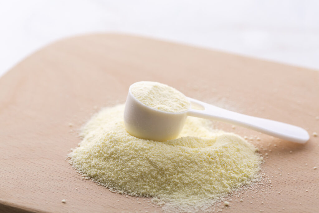 Baby formula fills a white plastic scoop on a wooden table.