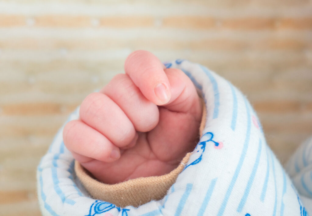 Sleeping newborn boy's hand is shown in a sleeve.