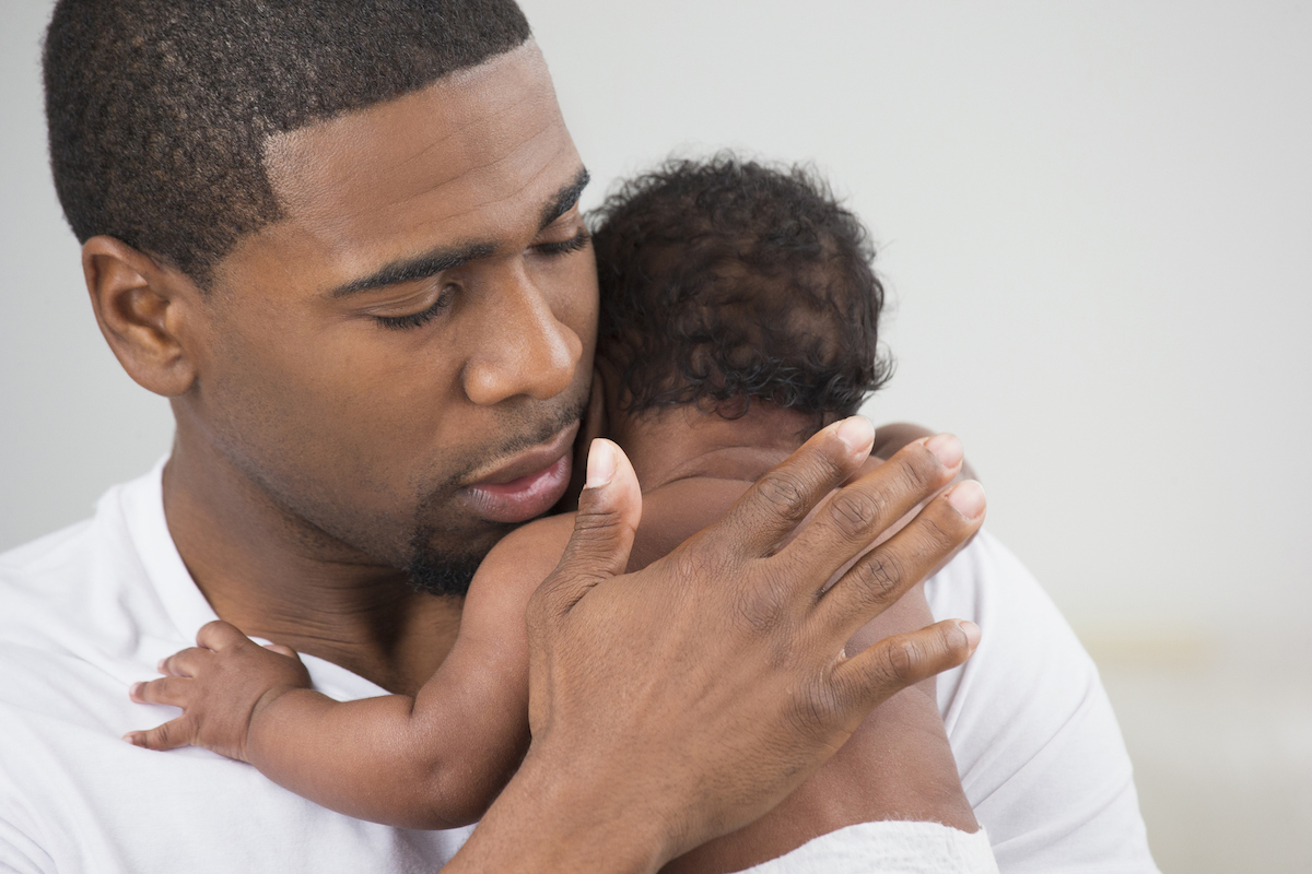 A parent holds a newborn and pats its back to burp it.