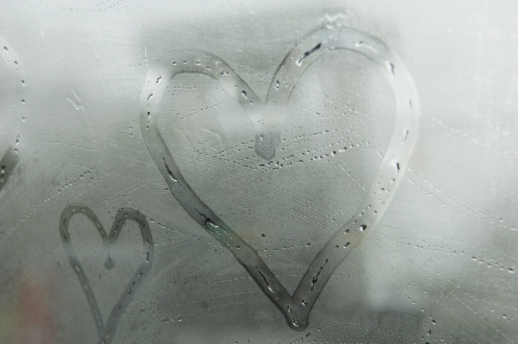 A big heart and a small heart are drawn in the steam on the mirror in a bathroom after a hot bath.