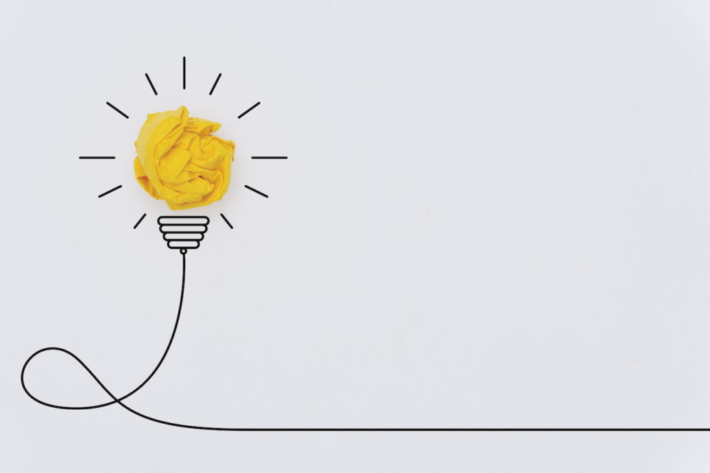 A lightbulb is made of crumpled yellow paper, with the other parts of the lightbulb drawn by hand.