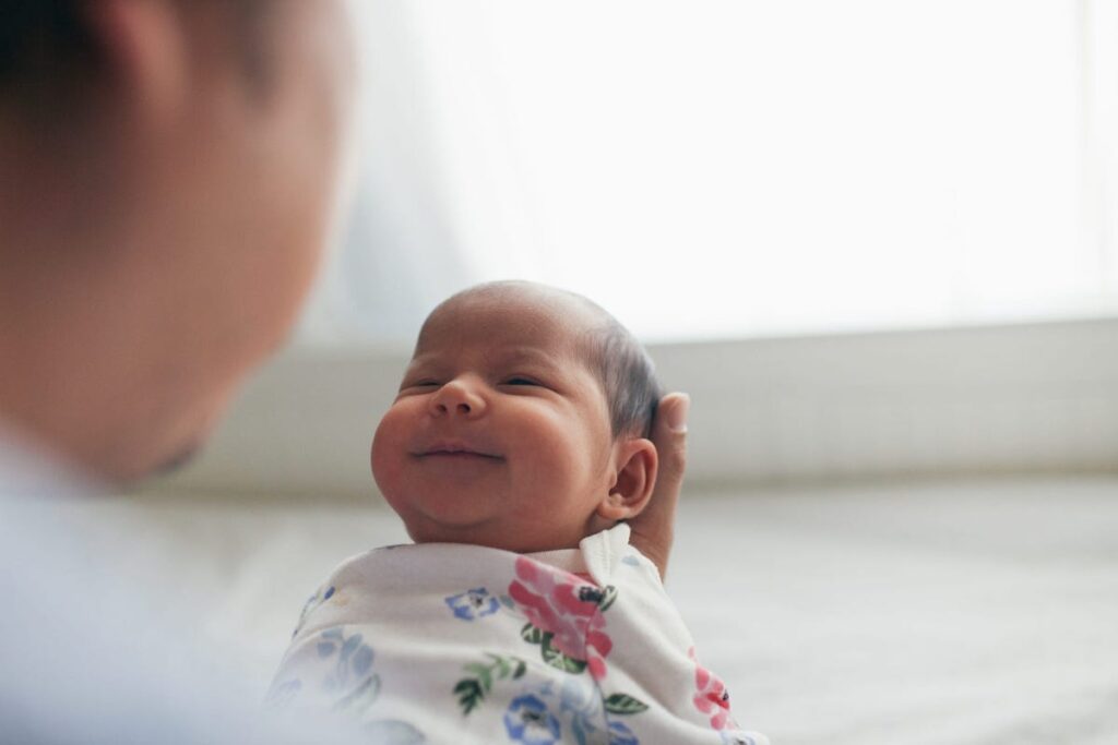 A baby smiles as it is held by a new father.