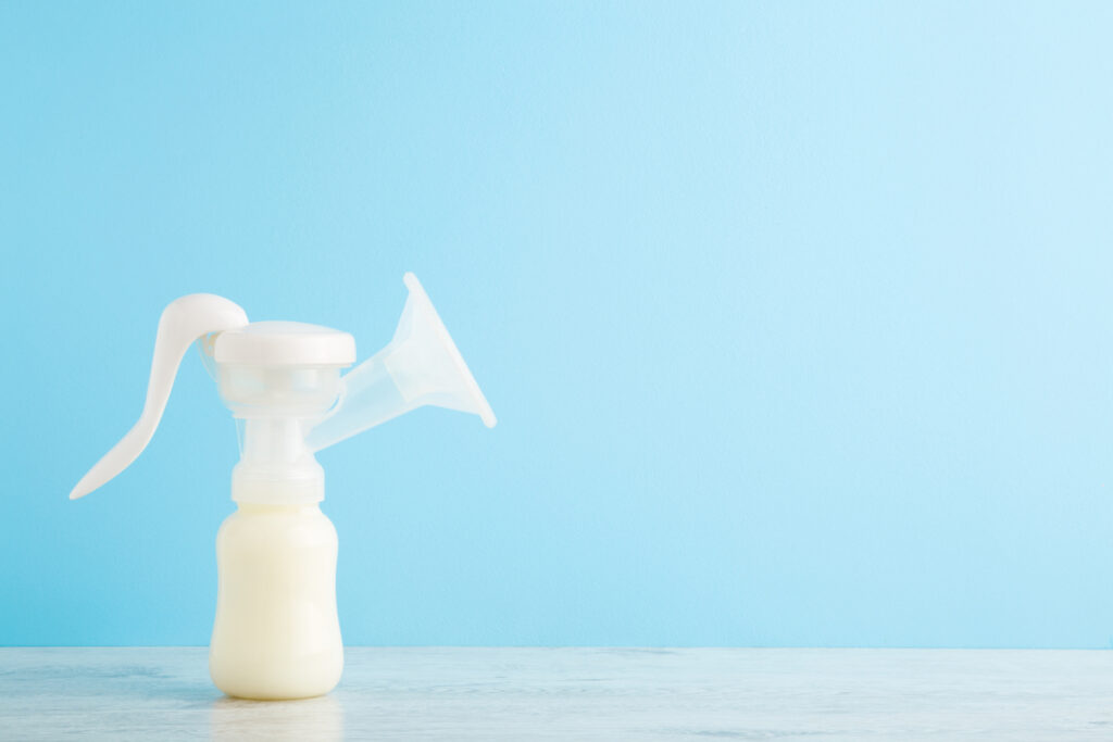 A manual breast pump filled with milk sits on a wooden table in front of a light blue wall.