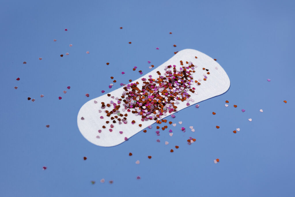 A white sanitary pad covered in red glitter on a blue background.