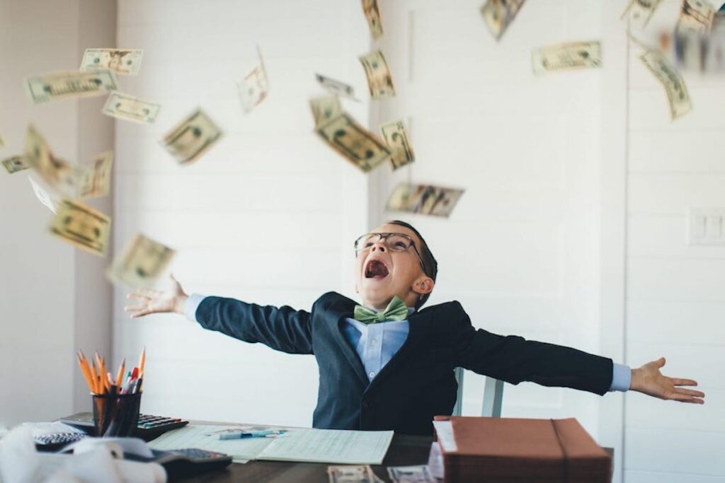 A boy wearing a suit and glasses throws dollar bills into the air.