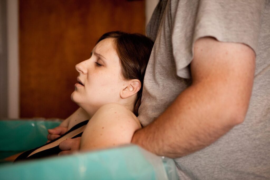 A pregnant person is supported by a partner in a pool of water for a water birth.