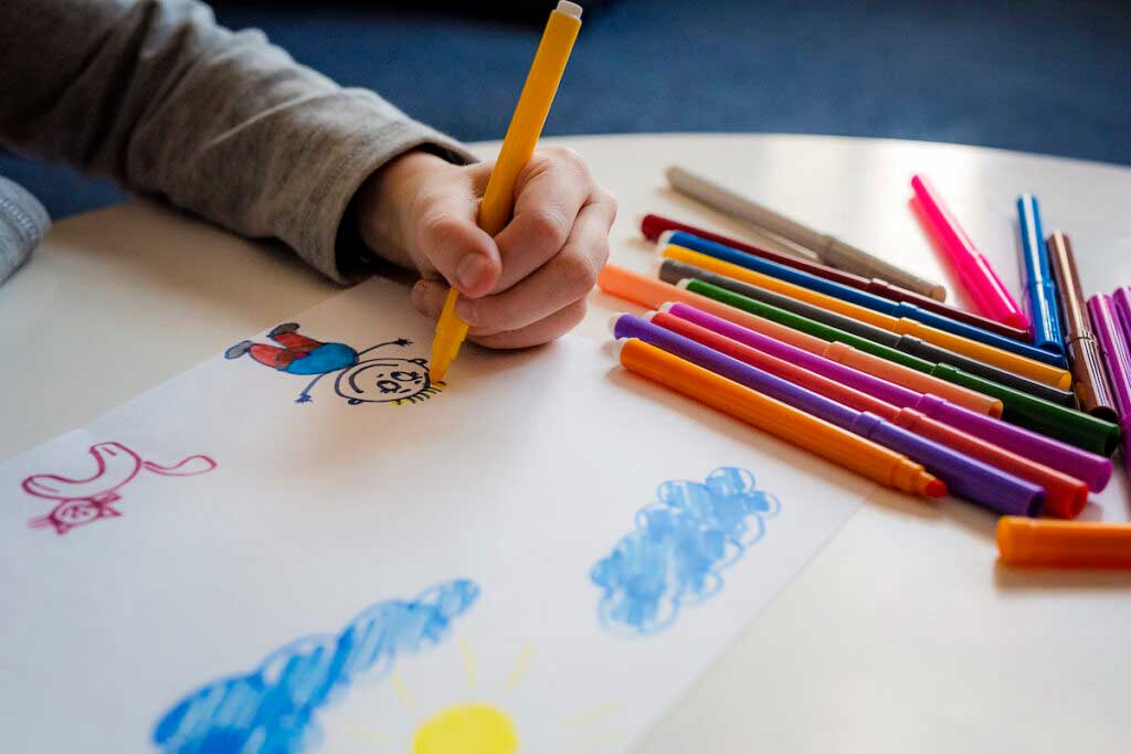 A left-handed child draws smiling figures with colored pencils.