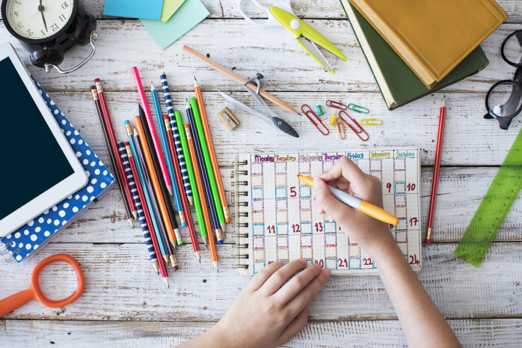 A calendar with colorful pens beside it.