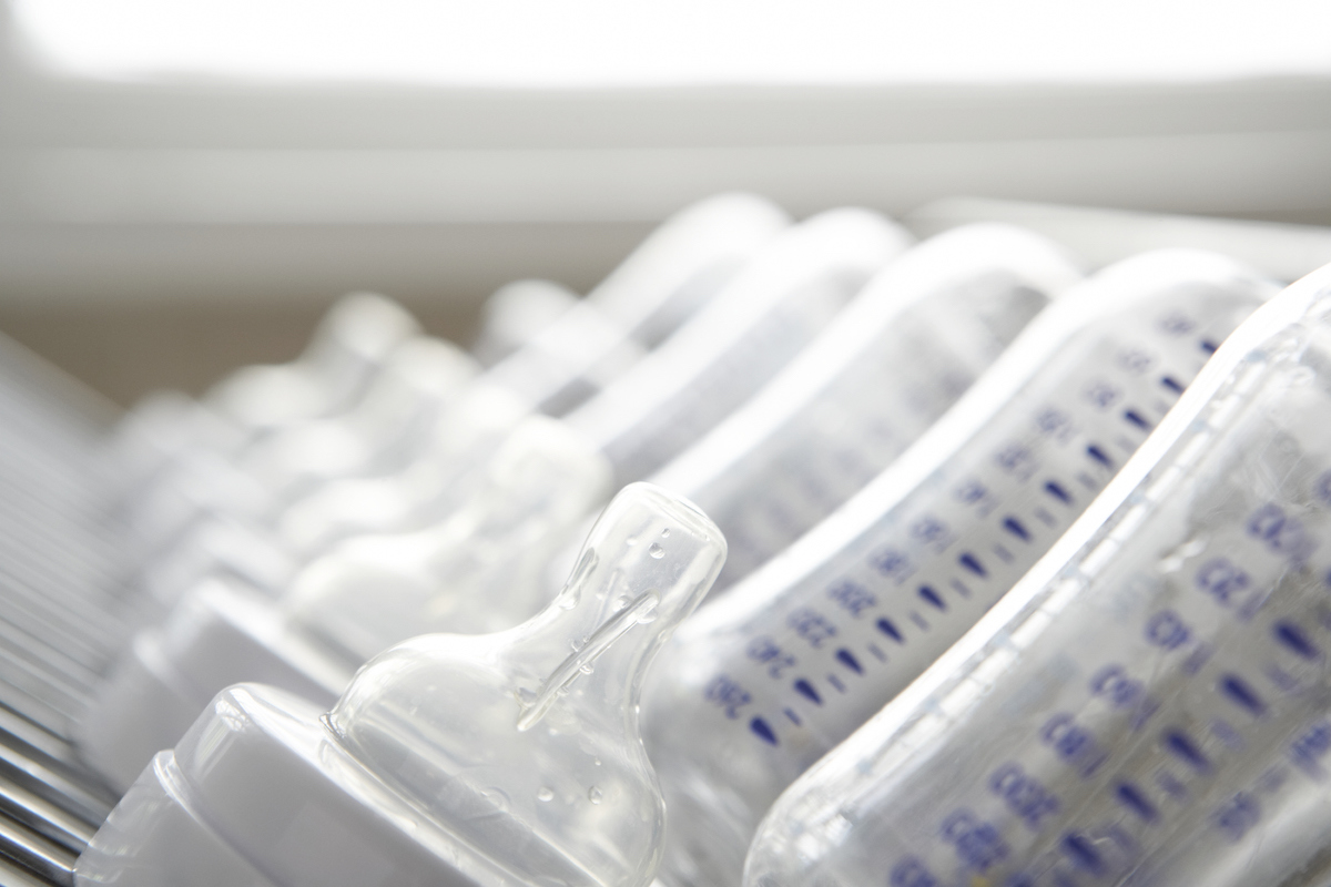 A close up of a row of plastic bottles and nipples arranged in a dishwasher.