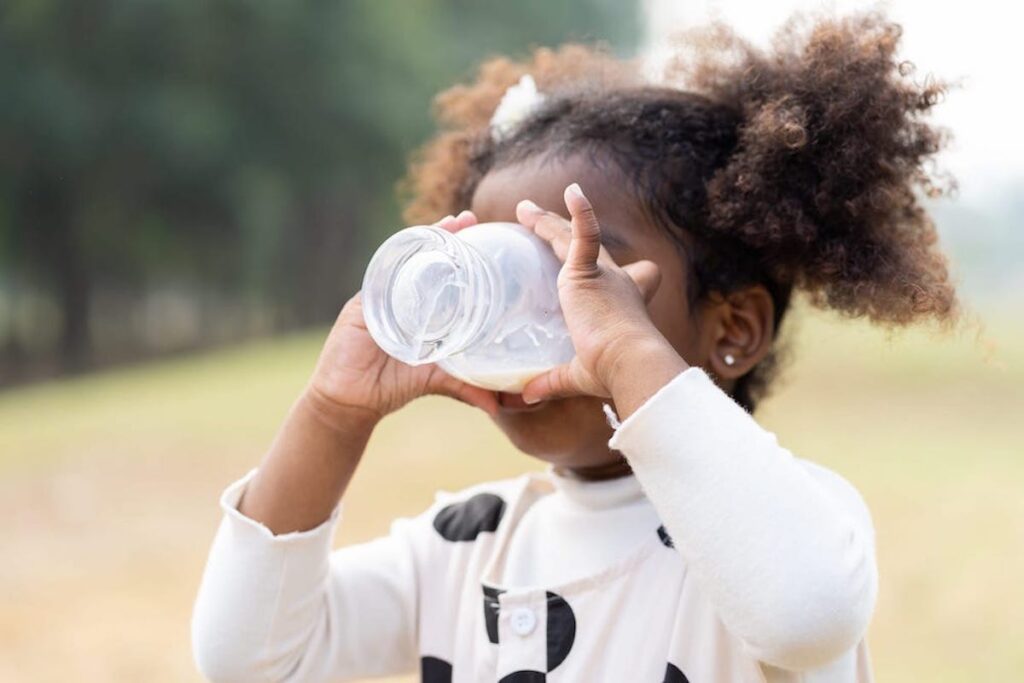 A young child drinks a glass of milk outdoors.