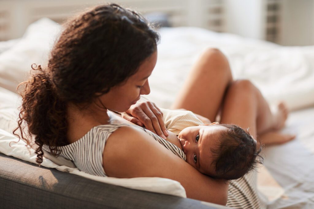 A young parent breastfeeds their baby on a bed.