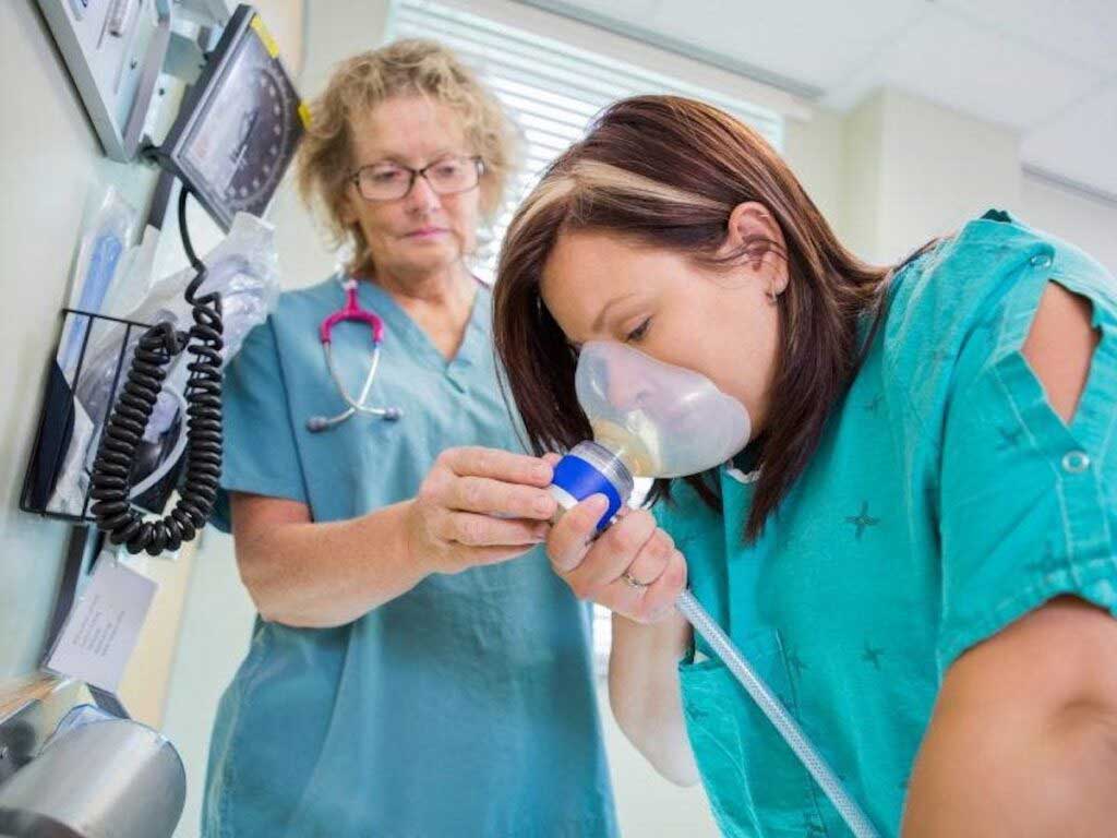 Pregnant person breathes nitrous through a mask while in labor in a hospital.