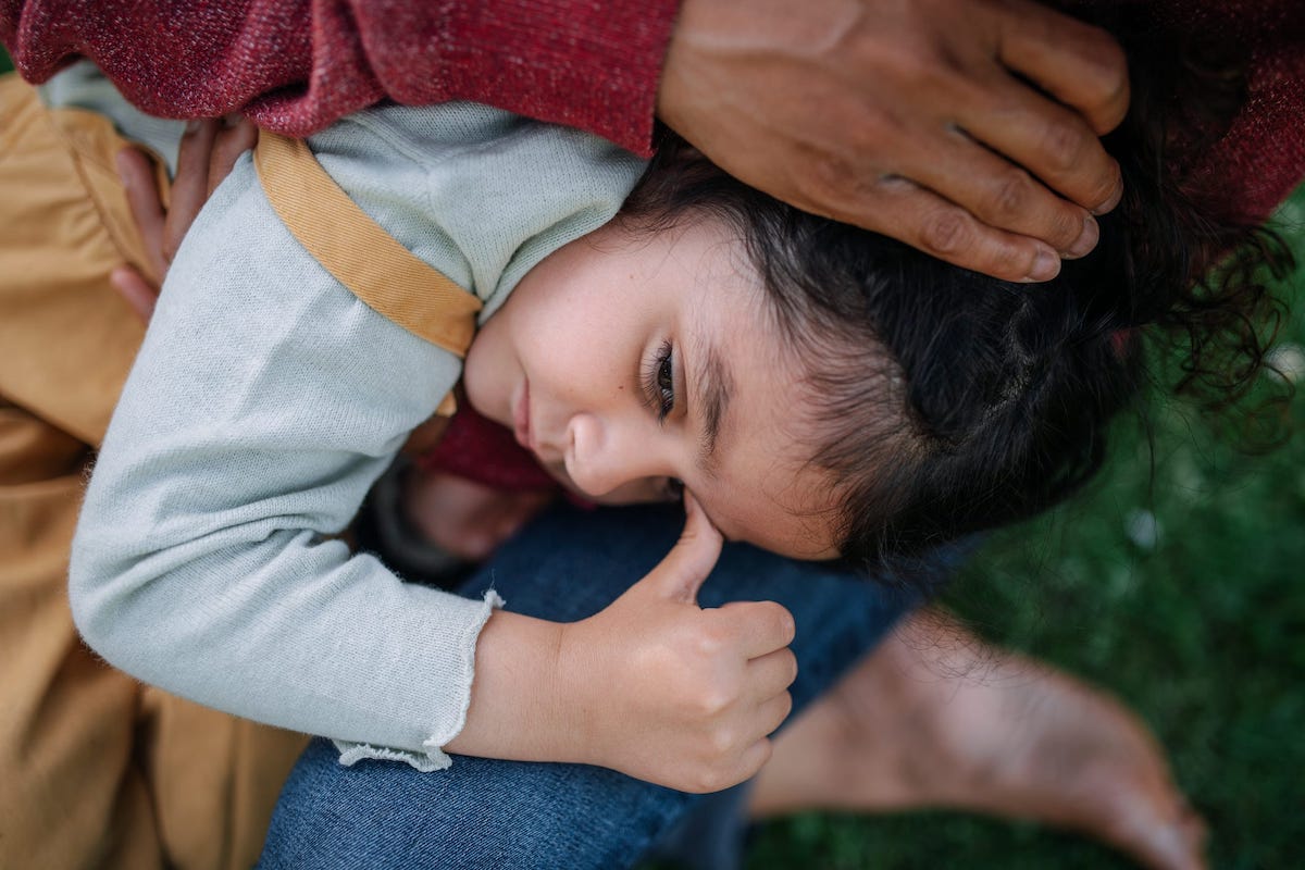 A child lays her head in the lap of a parent.