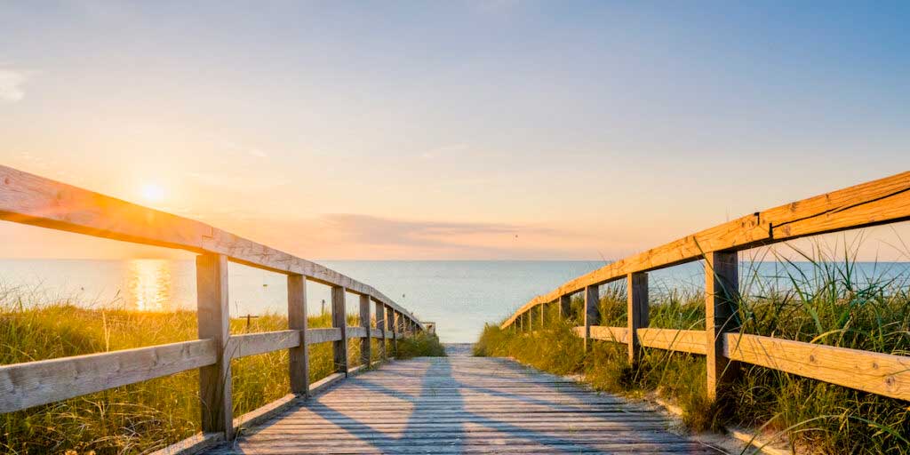 A wooden walkway leads to the sea at sunset.