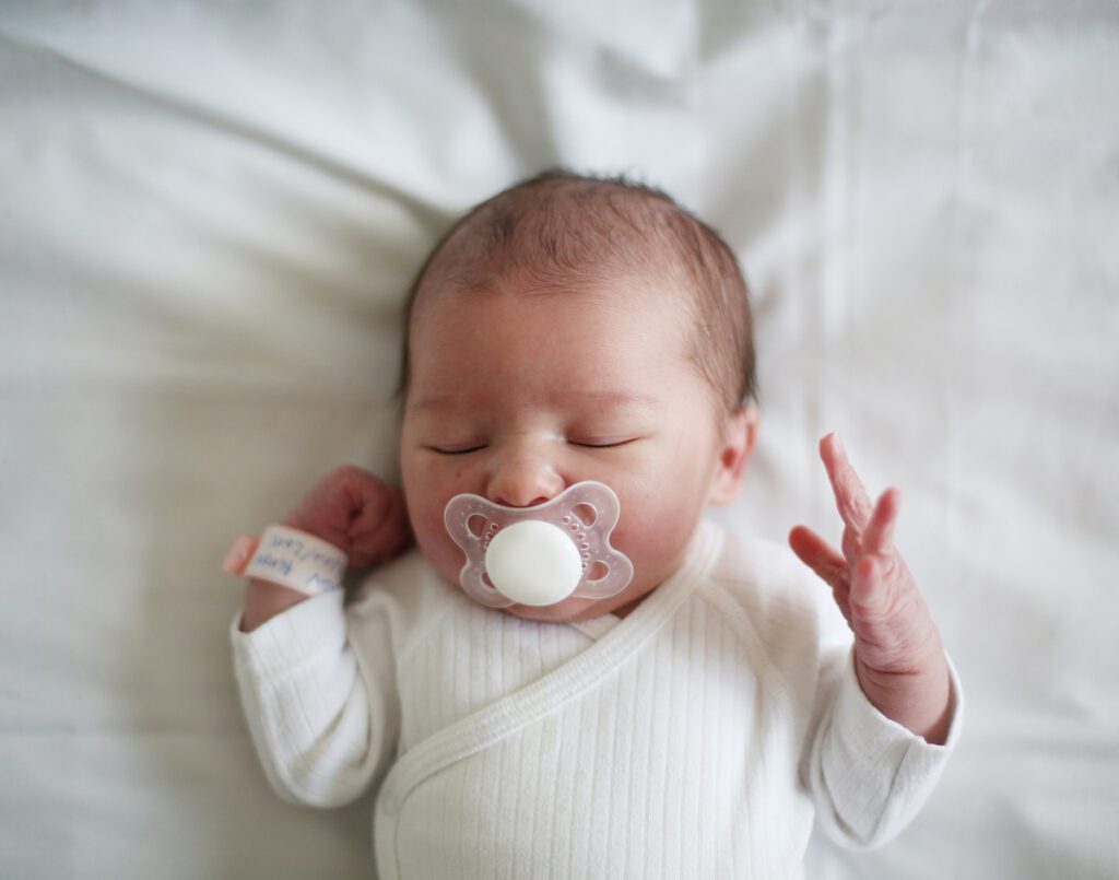 A newborn sleeps on their back sucking a pacifier.