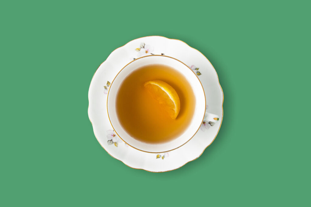 A dainty white cup of tea with a slice of lemon seen from overhead on a green background.