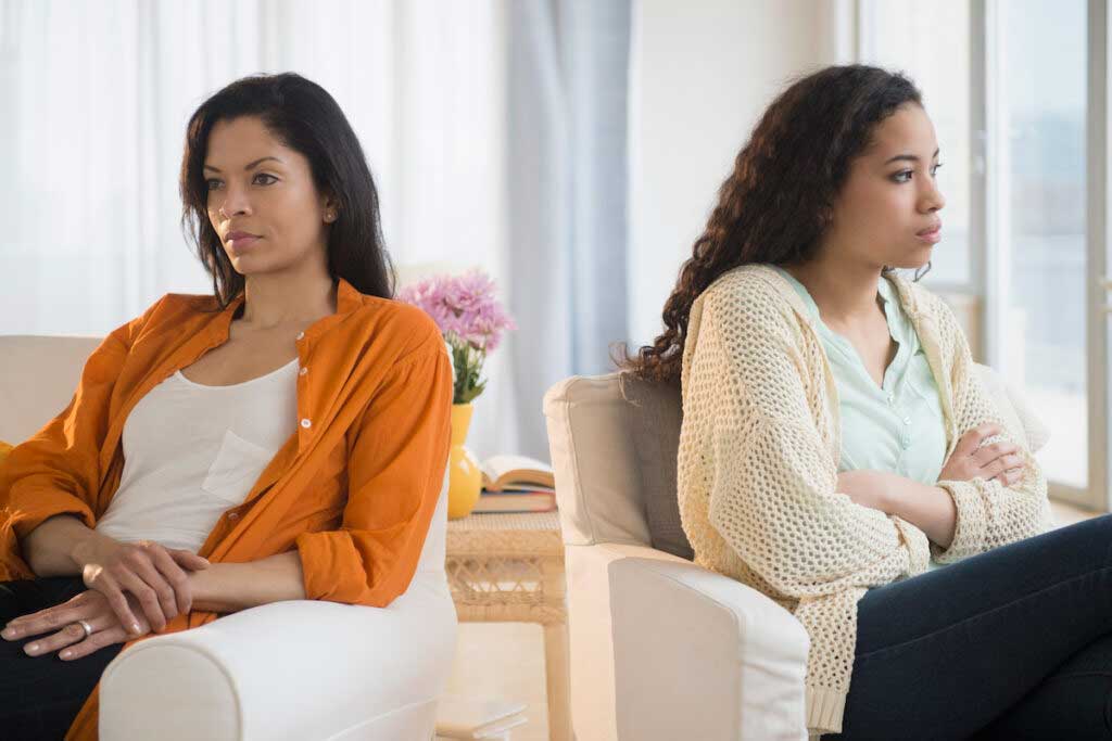 A parent and older child argue in their livingroom.