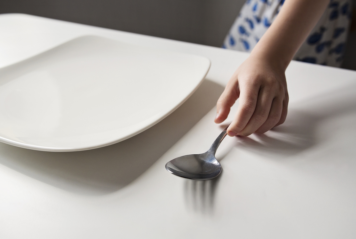 Close up of a child sitting at a table in front of an empty plate.