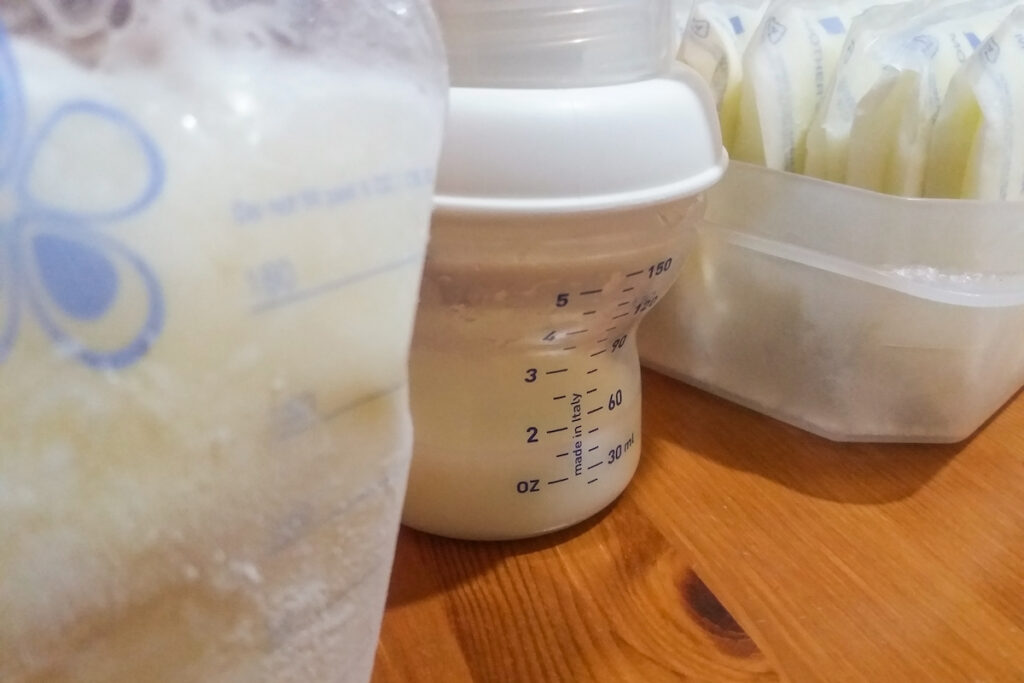 Frozen breast milk sits next to a bottle and a pump on a table.