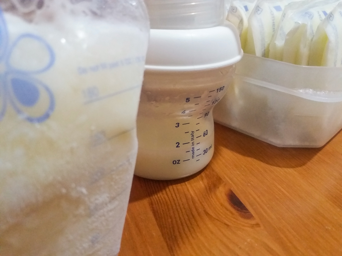 Frozen breast milk sits next to a bottle and a pump on a table.