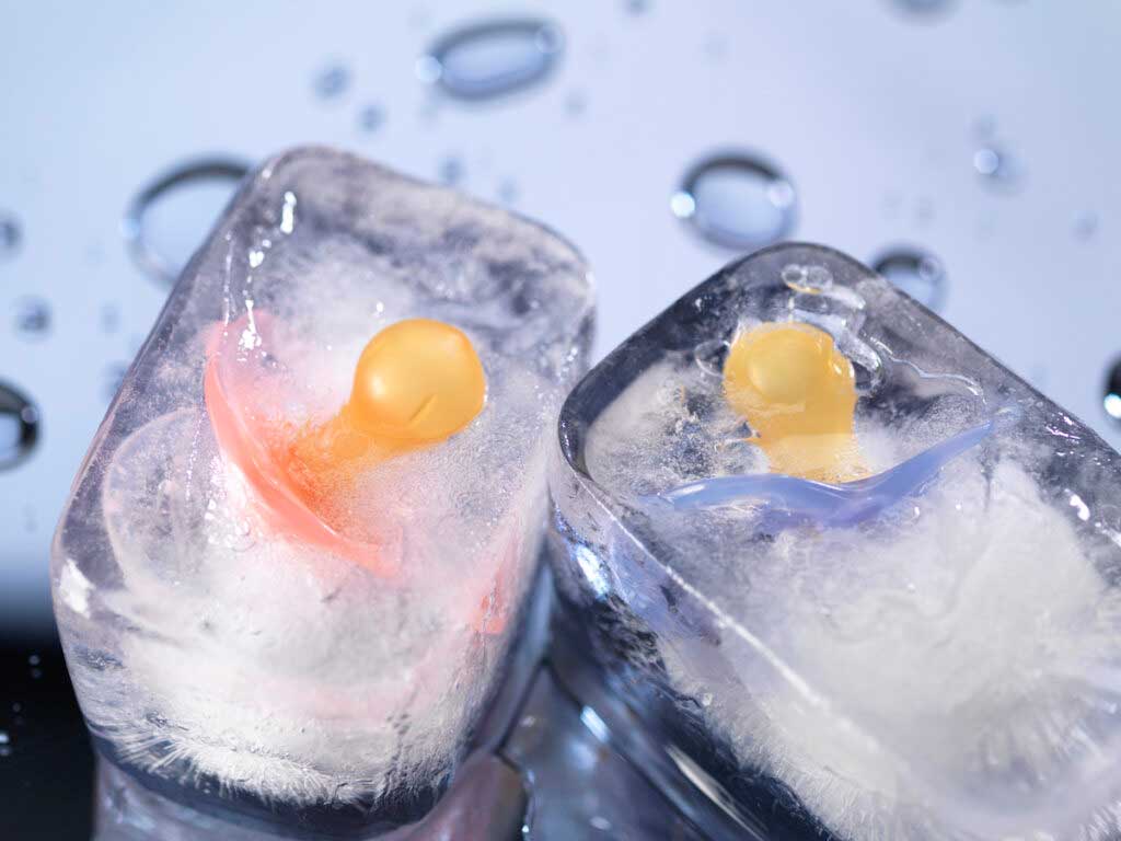 A pink and a blue pacifier frozen in two ice cubes.